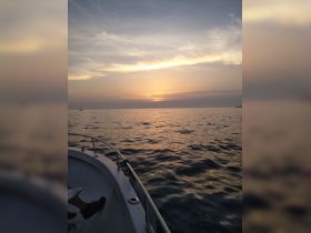 A serene sunset view from a boat, capturing the tranquil waters and the silhouette of another vessel in the distance — perfect for romantic evening cruises.