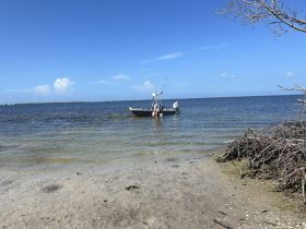 A small boat is anchored near the shore, with people enjoying the beautiful beach and water scenery — a perfect spot for relaxation and exploration.