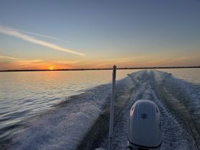 A serene sunset view from the back of a boat, showcasing the tranquil waters and beautiful sky, perfect for evening cruises.