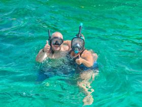 A joyful couple enjoys snorkeling in crystal-clear waters, giving thumbs up to capture the excitement of their underwater adventure.