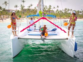 A lively group celebrates aboard a catamaran, enjoying drinks and the beach backdrop — perfect for festive outings and summer fun on the water.