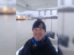 A smiling individual poses for a selfie on a boat, showcasing the surrounding water and nearby structures — perfect for capturing memorable moments on the water.