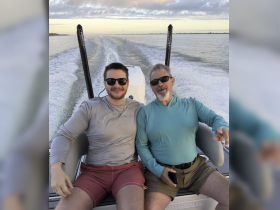A joyful moment shared between two men on a boat, enjoying a scenic cruise as the sun sets in the background — perfect for family outings or memorable adventures on the water.