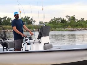 A man stands at the helm of a fishing boat, ready for a day on the water. Perfect for fishing enthusiasts looking to enjoy the great outdoors.