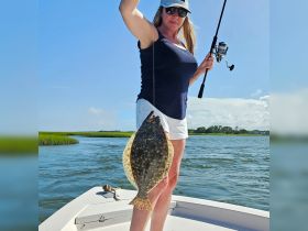 A woman proudly displays her catch of a flounder while fishing from a boat, showcasing the excitement of a successful day on the water.