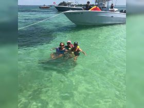 A joyful group of friends enjoys a refreshing swim in crystal-clear waters, with a boat anchored nearby — perfect for a fun day on the water.