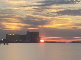 A sunset view over the water with buildings in the background, but the image is unclear and lacks distinct features.