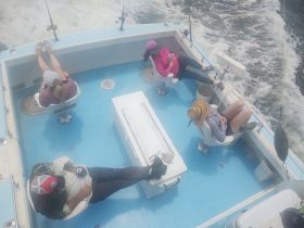 A group relaxes in the interior of a fishing boat, showcasing comfortable seating and a laid-back atmosphere while enjoying their time on the water.
