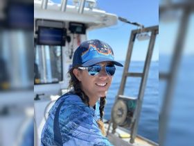 A smiling woman at the helm of a fishing boat, showcasing the excitement of a day on the water. Perfect for fishing enthusiasts and adventure seekers.