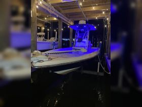 A sleek boat docked under a wooden structure, illuminated by ambient lighting at night, showcasing its design and features.