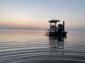 A serene view of a boat anchored at dusk, reflecting the beautiful colors of the sunset on calm waters — perfect for evening cruises or fishing trips.
