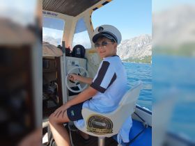 A young boy sits at the helm of a boat, wearing a captain's hat and sunglasses, ready to navigate the beautiful waters. Ideal for family boating adventures.