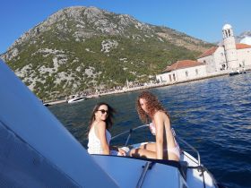 Two friends enjoy a sunny day on a boat, with stunning mountain and coastal scenery in the background — perfect for summer adventures on the water.
