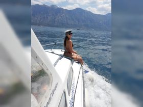 A woman enjoys a sunny day on a boat, smiling against a stunning mountainous backdrop — perfect for adventure seekers and boat tour enthusiasts.