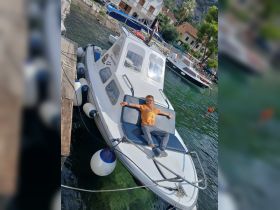 A child relaxes on the deck of a boat docked in a picturesque harbor, enjoying the serene waters and sunny day.