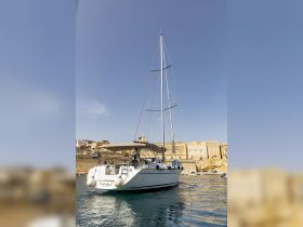 The yacht 'Farfalla I' is seen underway in the harbor, showcasing its elegant design against a historic backdrop.