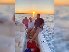 A group of friends enjoys a sunset cruise on a boat, capturing the perfect moment with drinks in hand as the sun sets over the horizon.
