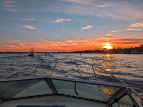 A stunning sunset view from the bow of a boat, showcasing the tranquil waters and other vessels in the distance — perfect for evening cruises.