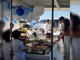 A vibrant buffet setup featuring a variety of food and drinks, perfect for celebrations on a boat. Guests, including a child, enjoy the catering in a festive atmosphere.