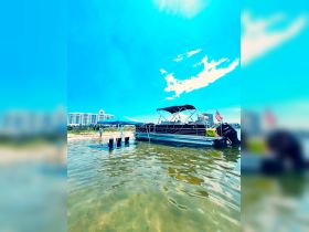 A group enjoys a sunny day at the beach with a pontoon boat anchored nearby, creating the perfect setting for relaxation and fun in the water.