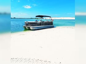 A pontoon boat is docked on a sandy shore, surrounded by clear blue waters, perfect for a day of relaxation and fun on the water.