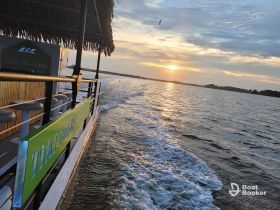 A scenic view of a tiki boat cruising at sunset, showcasing the tranquil waters and vibrant sky — perfect for sunset cruises and leisurely outings.