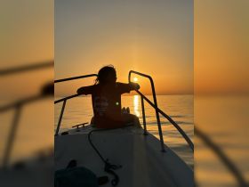 A child enjoys a serene sunset view from the bow of a boat, creating a beautiful silhouette against the vibrant sky — a perfect moment for family outings on the water.