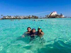 A joyful group of friends enjoys a refreshing swim in the crystal-clear waters, surrounded by a beautiful beach backdrop — perfect for family outings and snorkeling adventures.