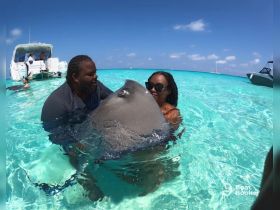 A couple interacts with a stingray in the crystal-clear waters, showcasing an unforgettable wildlife experience in the Bahamas.