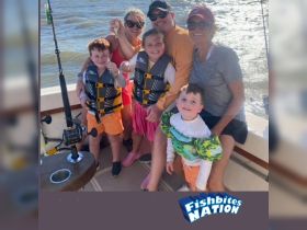 A joyful family poses on a fishing boat, showcasing their catch and enjoying a fun day on the water — perfect for family fishing adventures.
