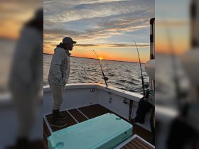 A man enjoys a peaceful fishing experience at sunset, casting his line into the shimmering ocean waters — a perfect moment for fishing enthusiasts.