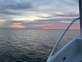 A serene sunset view from the deck of a boat, showcasing calm waters and a beautiful sky — perfect for evening cruises.