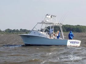 A fishing boat named 'Keeper' navigates through choppy waters with crew members on board, showcasing an adventurous day on the ocean.