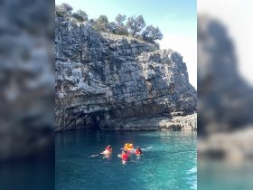 A group of swimmers in life jackets enjoys a refreshing swim near a rocky cave, showcasing the beauty of outdoor adventures and snorkeling experiences.