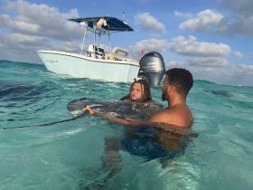 Two individuals interact with a stingray in the clear waters, showcasing a unique wildlife experience in a tropical setting.