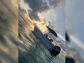 A serene view of a boat at sunset, showcasing its sleek design against a backdrop of colorful clouds and shimmering water — perfect for a peaceful day on the water.