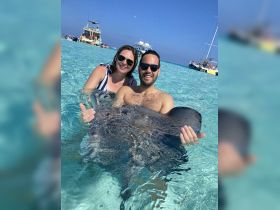 A couple interacts with a stingray in the clear waters, showcasing a unique wildlife experience in a tropical paradise.