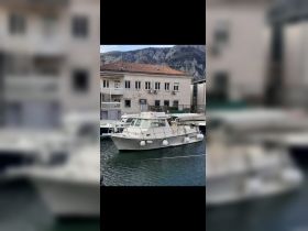 A well-maintained boat docked at a marina, showcasing its sleek design against a scenic backdrop of mountains and buildings.