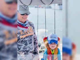 A joyful moment on the water as a child dressed as a captain enjoys a fishing trip with an adult, showcasing the fun of family boating adventures.