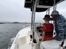 A father teaches his son how to navigate a boat, creating memorable moments on the water. Perfect for family bonding and learning experiences while boating.