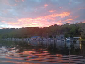 A stunning sunset over a tranquil harbor, showcasing boats lined up along the shore, perfect for capturing the beauty of nature and peaceful moments on the water.