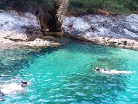 Two snorkelers explore the vibrant, clear waters near a rocky coastline, showcasing the beauty of underwater adventures in a stunning natural setting.