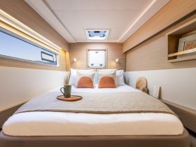 A cozy cabin interior featuring a comfortable bed with decorative pillows and a scenic window view, perfect for relaxing on a boat getaway.