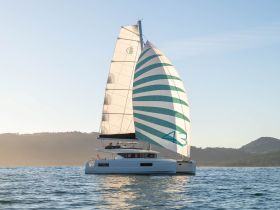 A stunning catamaran sails gracefully on calm waters, showcasing its vibrant striped sail against a serene backdrop — perfect for sailing enthusiasts and charter adventures.