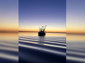 A serene silhouette of a fishing boat against a stunning sunset, reflecting on calm waters — a perfect scene for nature lovers and boating enthusiasts.