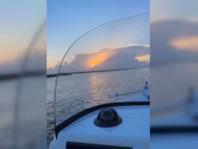 A serene sunset view from the dashboard of a boat, capturing the tranquil waters and vibrant sky — perfect for evening cruises.