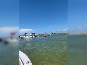 A lively scene at a sandbar with groups of people enjoying the water and several boats anchored nearby, perfect for a fun day out on the water.