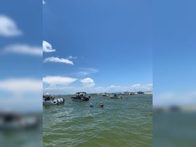 A lively scene at a sandbar with multiple boats and people enjoying swimming and relaxing in the water, perfect for a fun day out on the water.