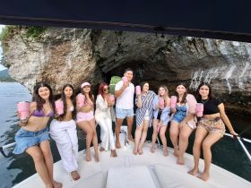 A lively group of friends enjoys cocktails on a boat, celebrating together against a stunning rocky backdrop — perfect for unforgettable summer outings.