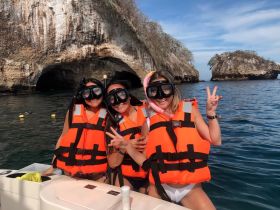 Three friends pose for a fun photo while snorkeling in the ocean, wearing bright life jackets against a stunning coastal backdrop.